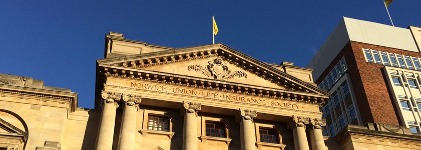 norwich A historic building with a stone facade, columns, and a triangular pediment displaying Norwich Union Life Insurance Society stands proudly. With a yellow flag fluttering under the clear blue sky, its an inspiring view akin to the innovative spirit of Glued Limited, the renowned marketing agency in Warwickshire.