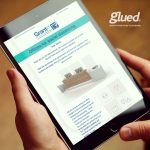 A person is holding a tablet displaying an email about office furniture for social distancing, featuring text and images of desks. The Glued logo proudly appears at the top right corner, showcasing the creative touch of Glued Marketing, a leading marketing agency in Warwickshire.