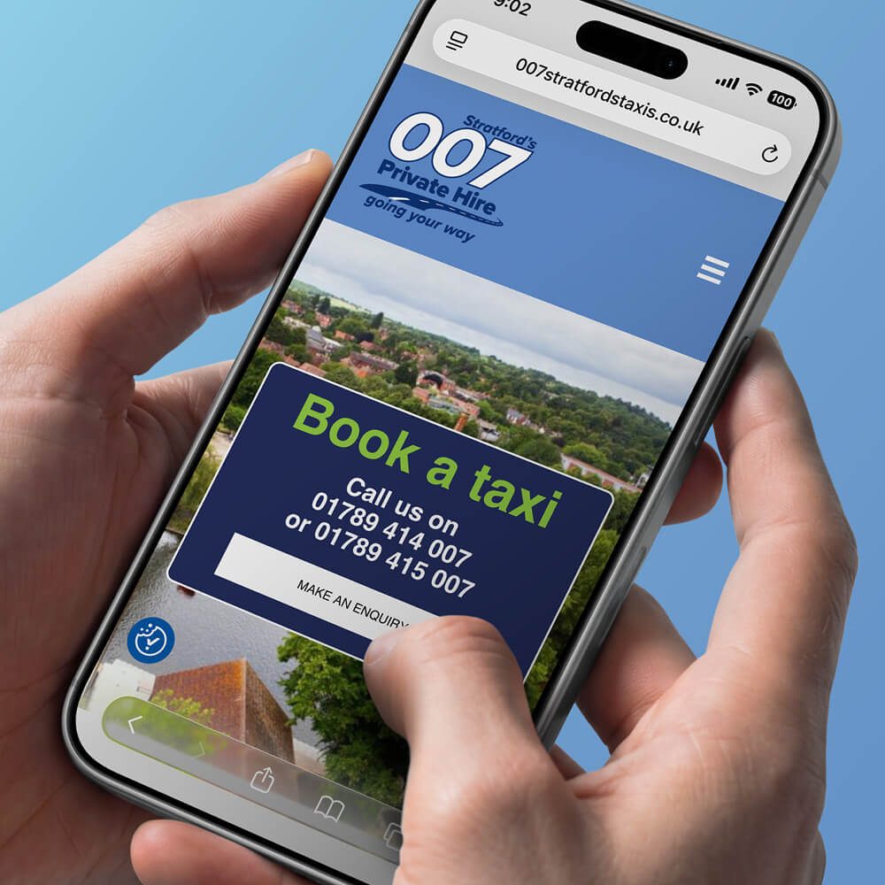 Glued Limited creative work: A hand holds a mobile displaying the 007 Stratford Taxis WordPress website design and build at affordable prices, featuring a “Book a taxi” button and contact phone numbers on the screen, set against a scenic town background.