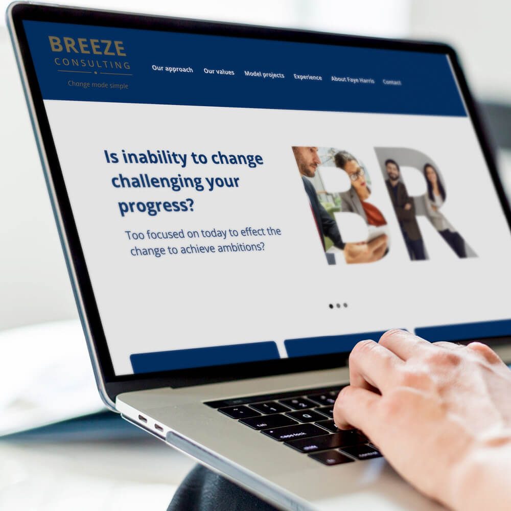 Glued Limited creative work: A person types on a laptop displaying the Breeze Consulting website, featuring a blue and white design created with Wordpress website design and build at affordable prices, company values, and the text “Is inability to change challenging your progress?”.