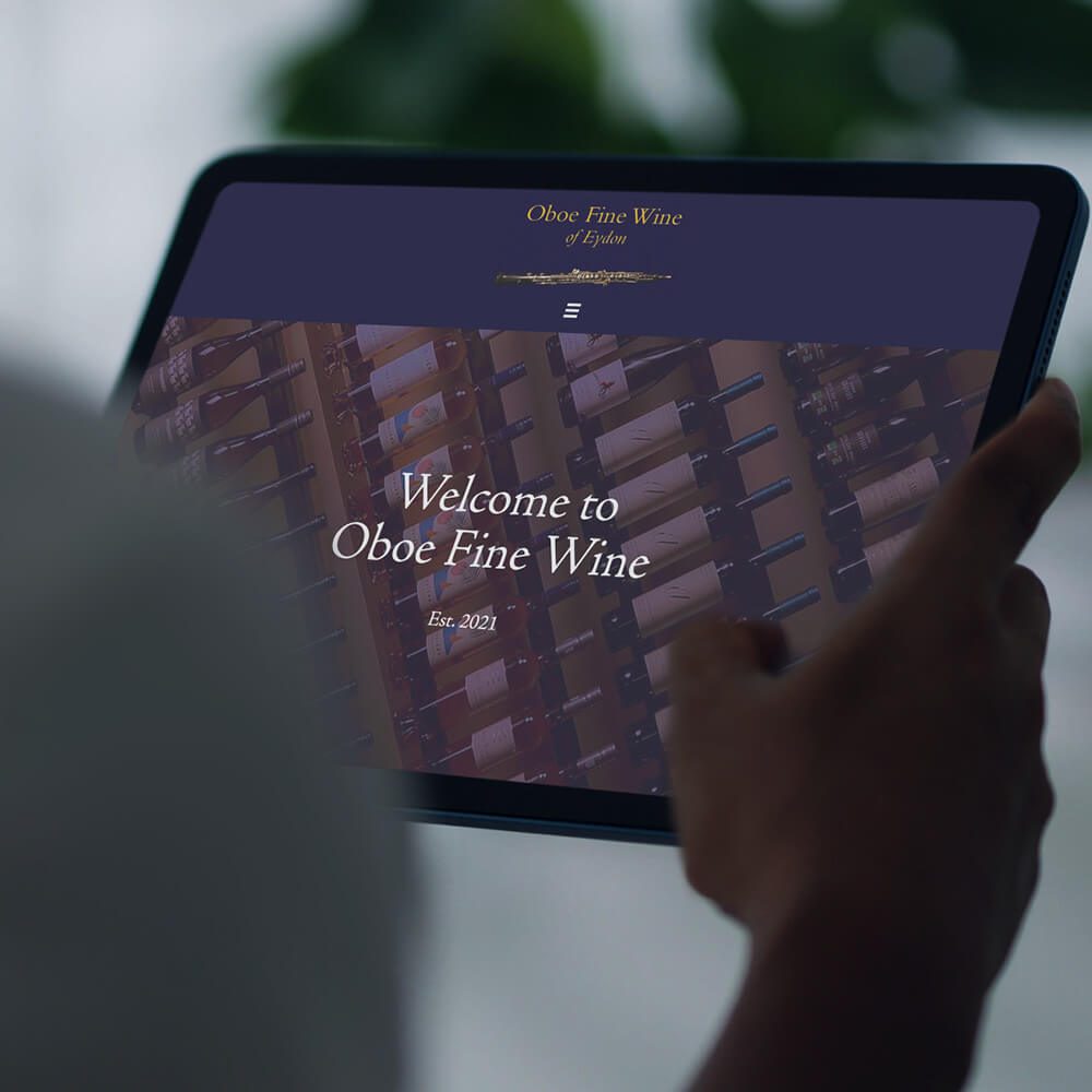 Glued Limited creative work: A person holding a tablet displaying the homepage of Oboe Fine Wine, created with WordPress website design and build at affordable prices, featuring wine bottles in a rack and the text Welcome to Oboe Fine Wine, Est. 2021.